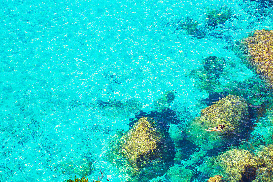 Person schwimmt im smaragdgrünen Wasser von Cala Mitjana, Menorca, Balearen. Spanien