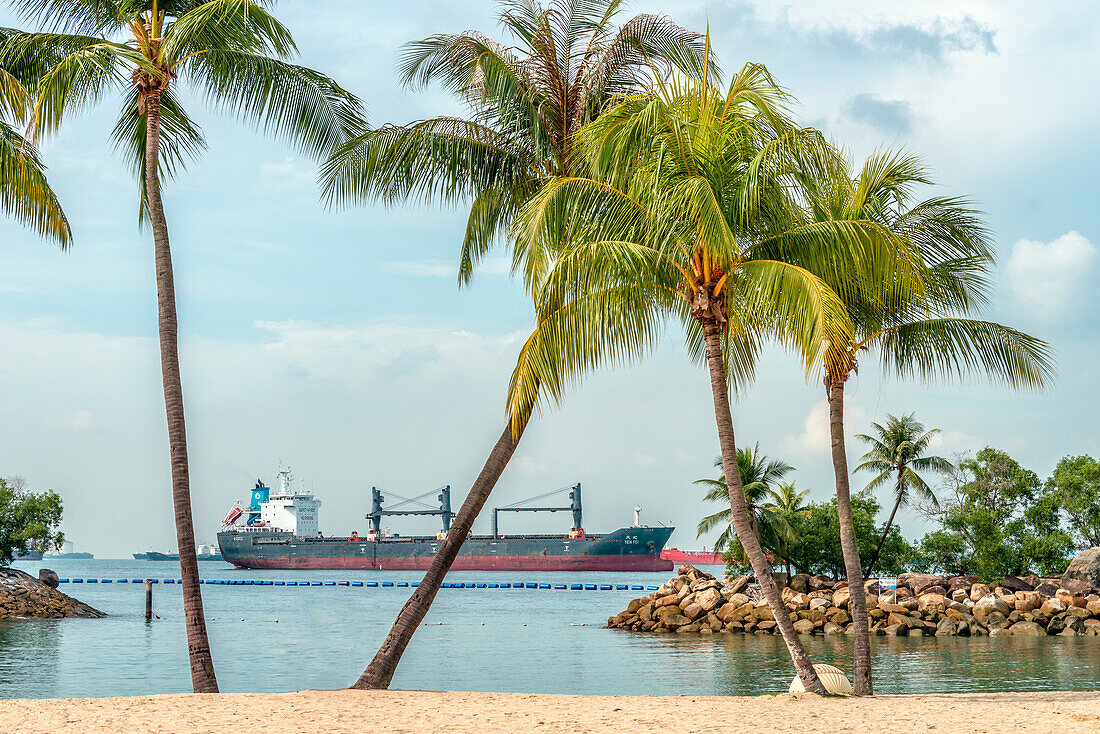 Palawan Strand auf der Insel Sentosa, mit einem Frachtschiff auf Reede in der Strasse von Singapur im Hintergrund, Singapur