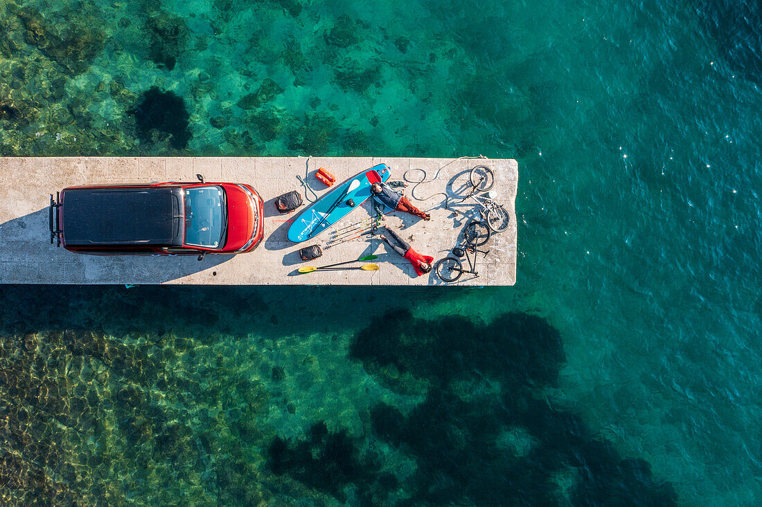 Road trip Croatia, two people with leisure equipment, bicycles, SUP board and camper on a jetty