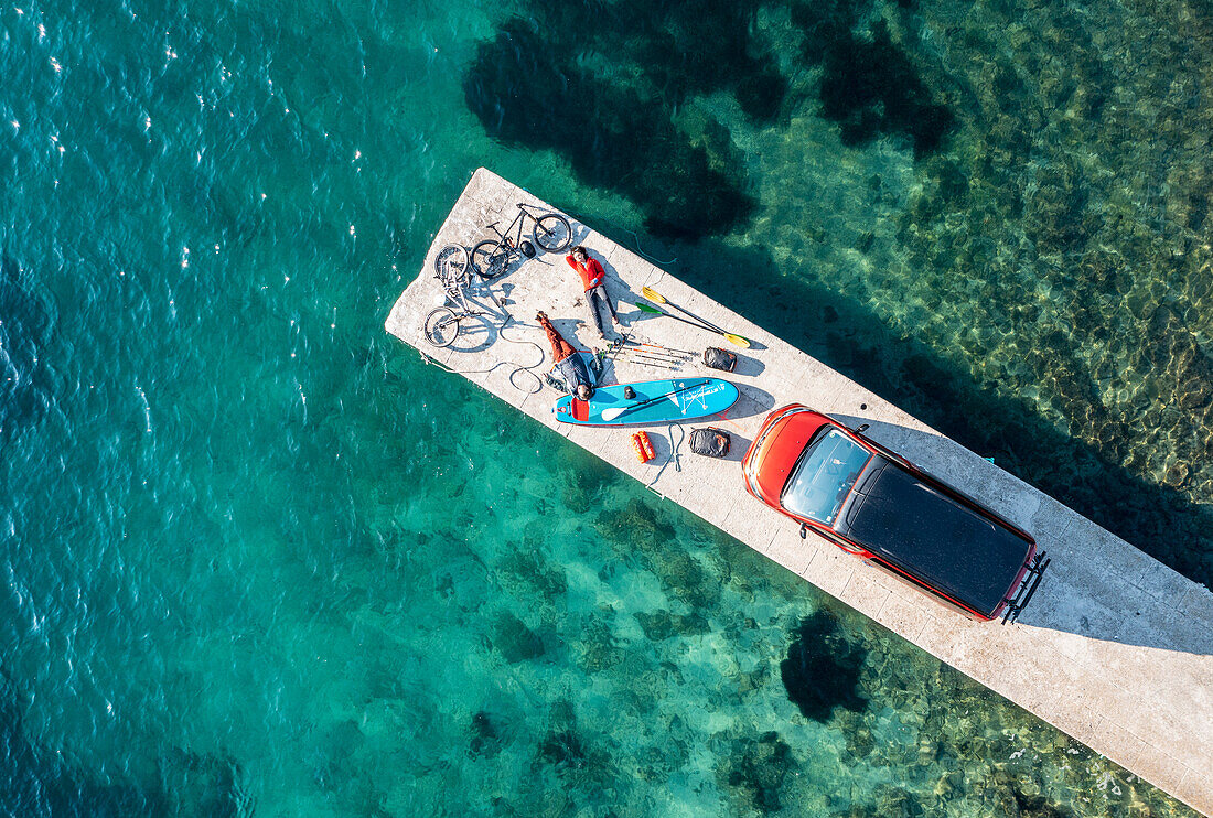 Road trip Croatia, two people with leisure equipment, bicycles, SUP board and camper on a jetty