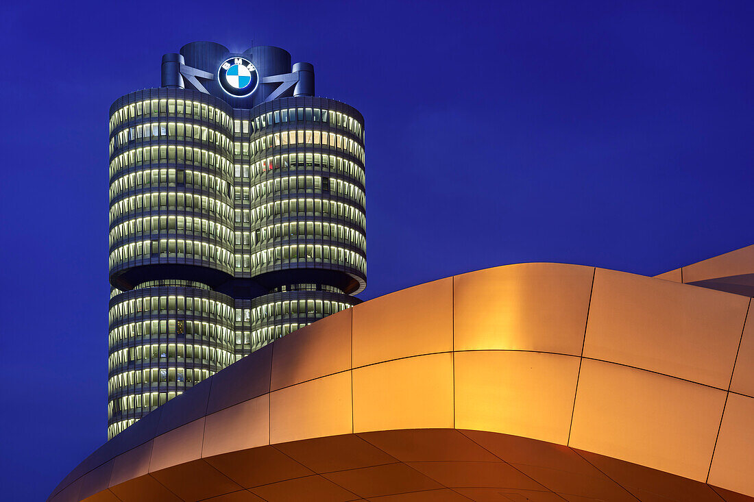Yellow illuminated BMW Welt building with BMW four-cylinder in the background, Munich, Upper Bavaria, Bavaria, Germany