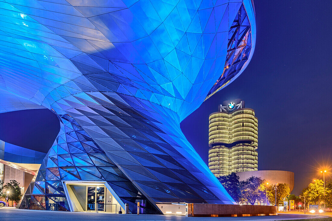 Blue illuminated BMW Welt building with BMW four-cylinder and BMW Museum in the background, Munich, Upper Bavaria, Bavaria, Germany