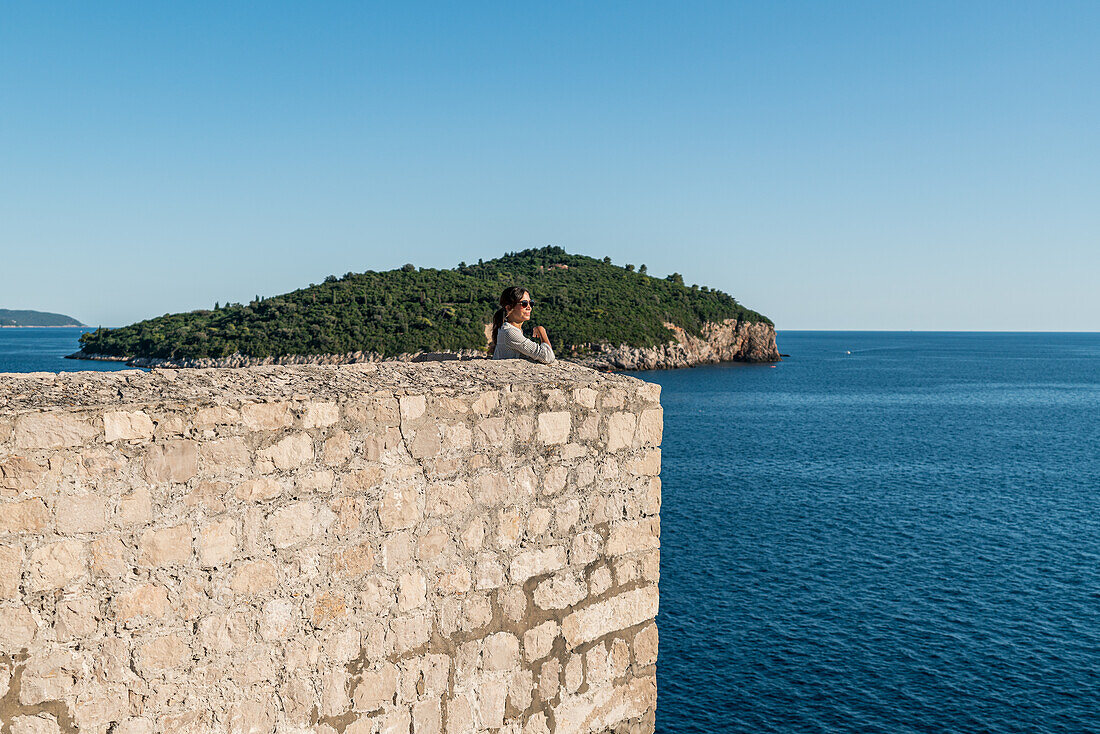 Frau blickt von den Stadtmauern der Altstadt aufs Meer hinaus in Dubrovnik, Dalmatien, Kroatien.