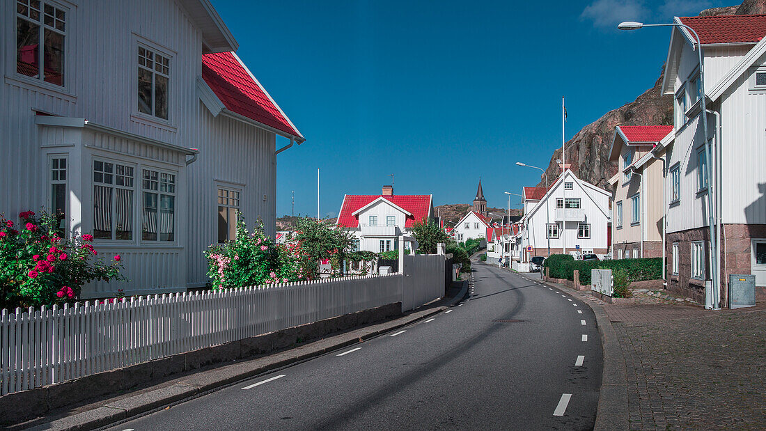 Street with white houses in the village of Fjällbacka by day with sun and blue sky on the west coast of Sweden