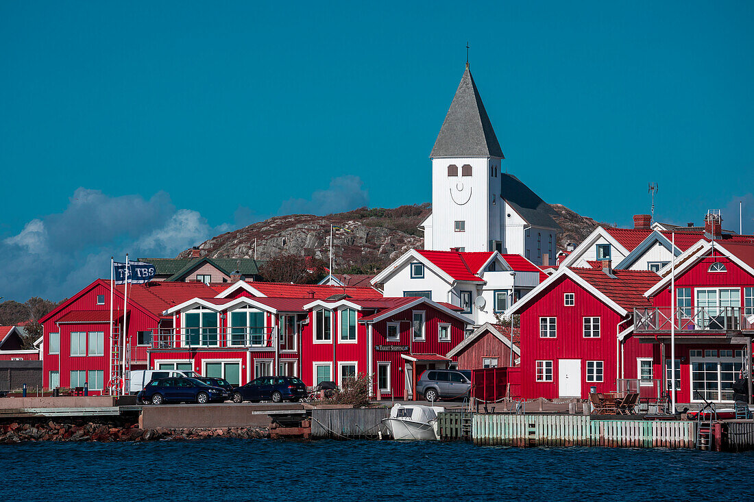 Rote Häuser mit Kirche im Dorf Skärhamn auf der Schäreninsel Tjörn an der Westküste von Schweden, blauer Himmel mit Sonne
