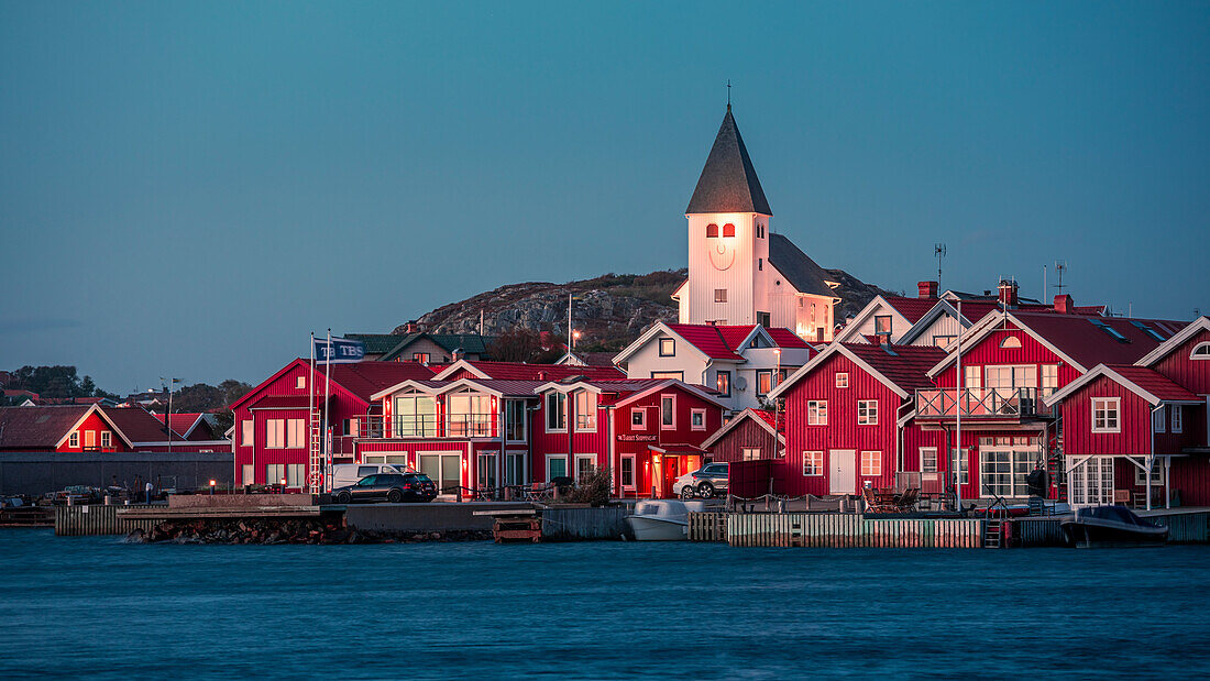 Rote Häuser mit Kirche im Dorf Skärhamn auf der Schäreninsel Tjörn an der Westküste von Schweden, am Abend\n
