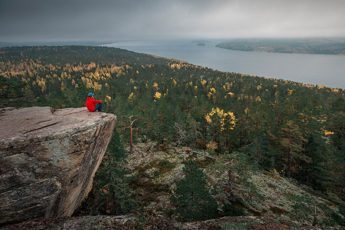 Mann auf der Felsklippe Predikstolen auf dem Getsvedjeberget mit Blick über die Landschaft von Höga Kusten im Osten von Schweden\n