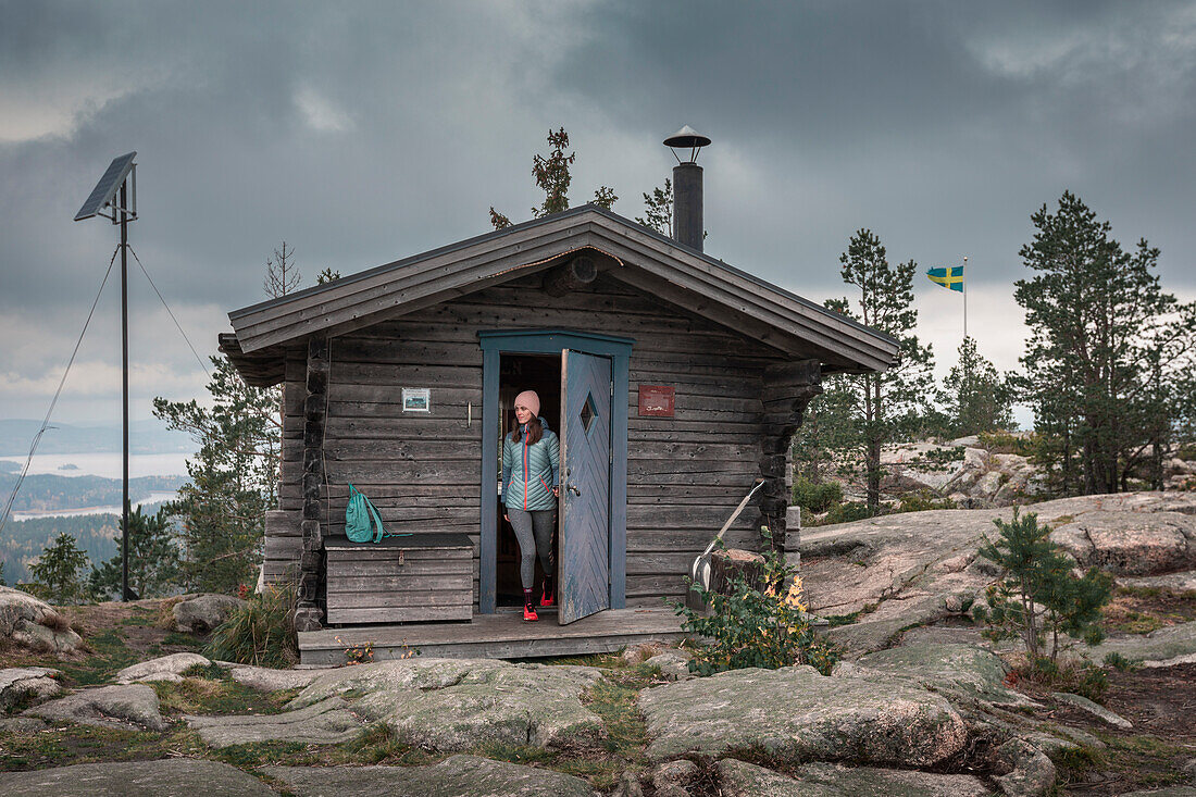 Frau öffnet Türe der Schutzhütte auf dem Gipfel des Valkallen in Höga Kusten im Osten von Schweden\n