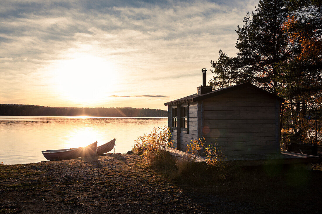 Hütte mit Booten am See in Lappland in Schweden im Sonnenuntergang\n