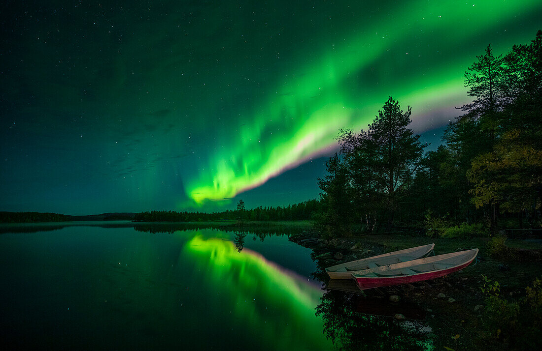 Polarlichter im Nachthimmel am Seeufer mit Booten in Lappland, Schweden\n