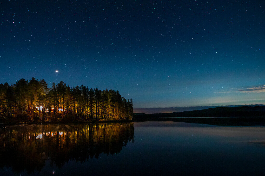 Forest by the lake under the starry sky at night in Lapland, Sweden