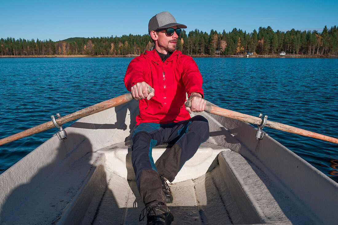 Man rowing in paddle boat on lake in Lapland with sun and blue sky