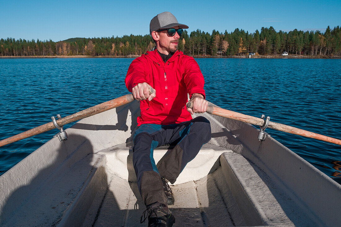 Mann rudert in Paddelboot auf See in Lappland bei Sonne und blauem Himmel\n