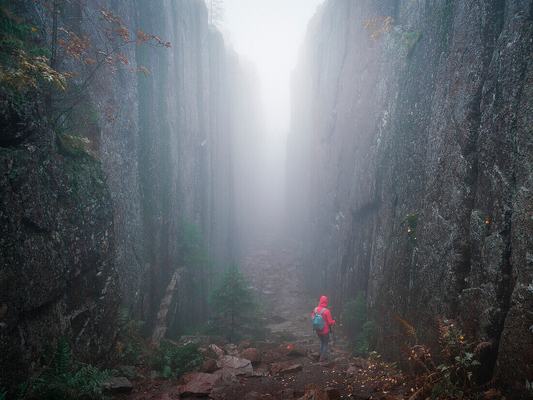 Woman hikes through Slåttdalsskrevan canyon with fog in Skuleskogen National Park in eastern Sweden