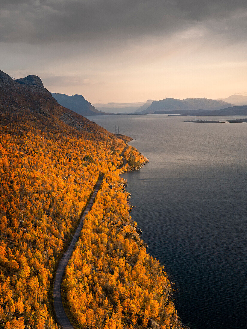 Road through landscape with mountains and lake in Stora Sjöfallet National Park in autumn in Lapland in Sweden from above