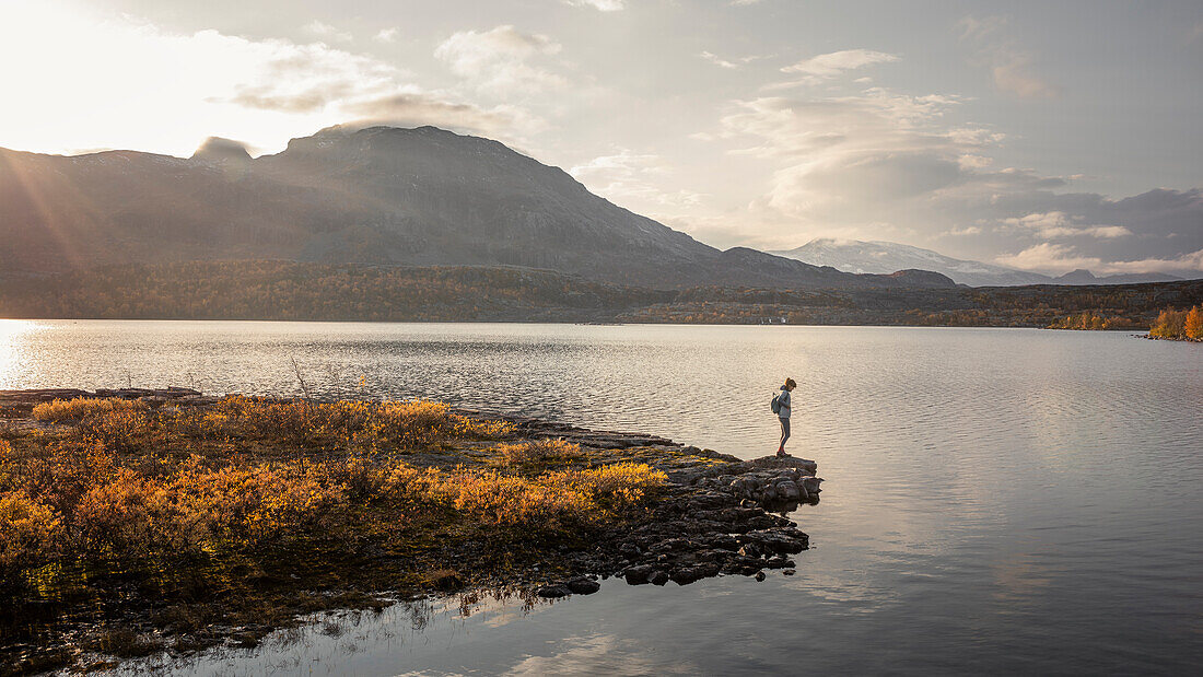 Frau in Landschaft mit Bergen und See im Stora Sjöfallet Nationalpark im Herbst in Lappland in Schweden\n