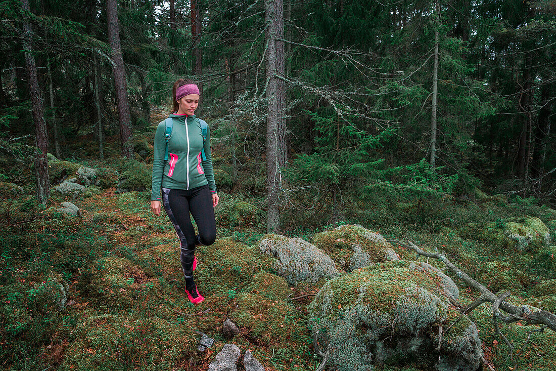 Frau wandert durch Wald mit Moos bedecktem Boden im Tyresta Nationalpark in Schweden
