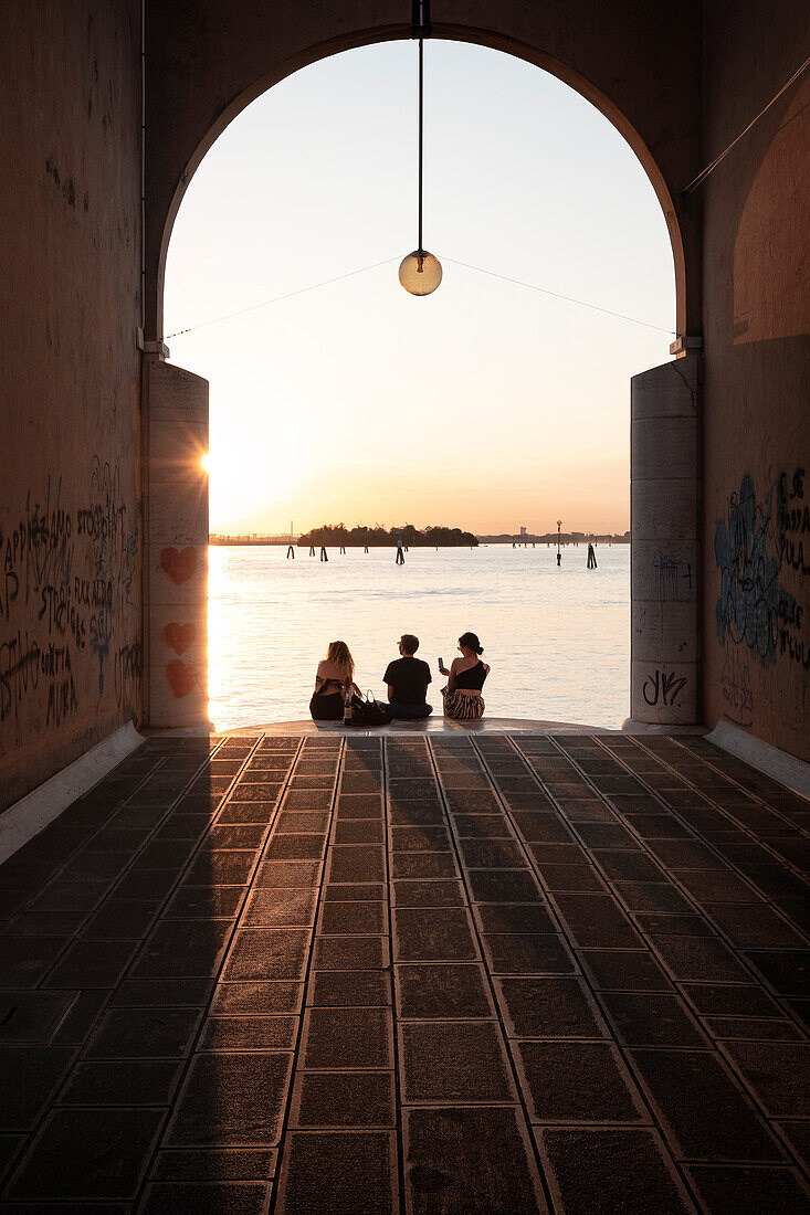 Leute sitzen zum Sonnenuntergang auf Stufen an einem Torbogen, Cannaregio, Venedig, Venezia, Venetien, Italien, Europa