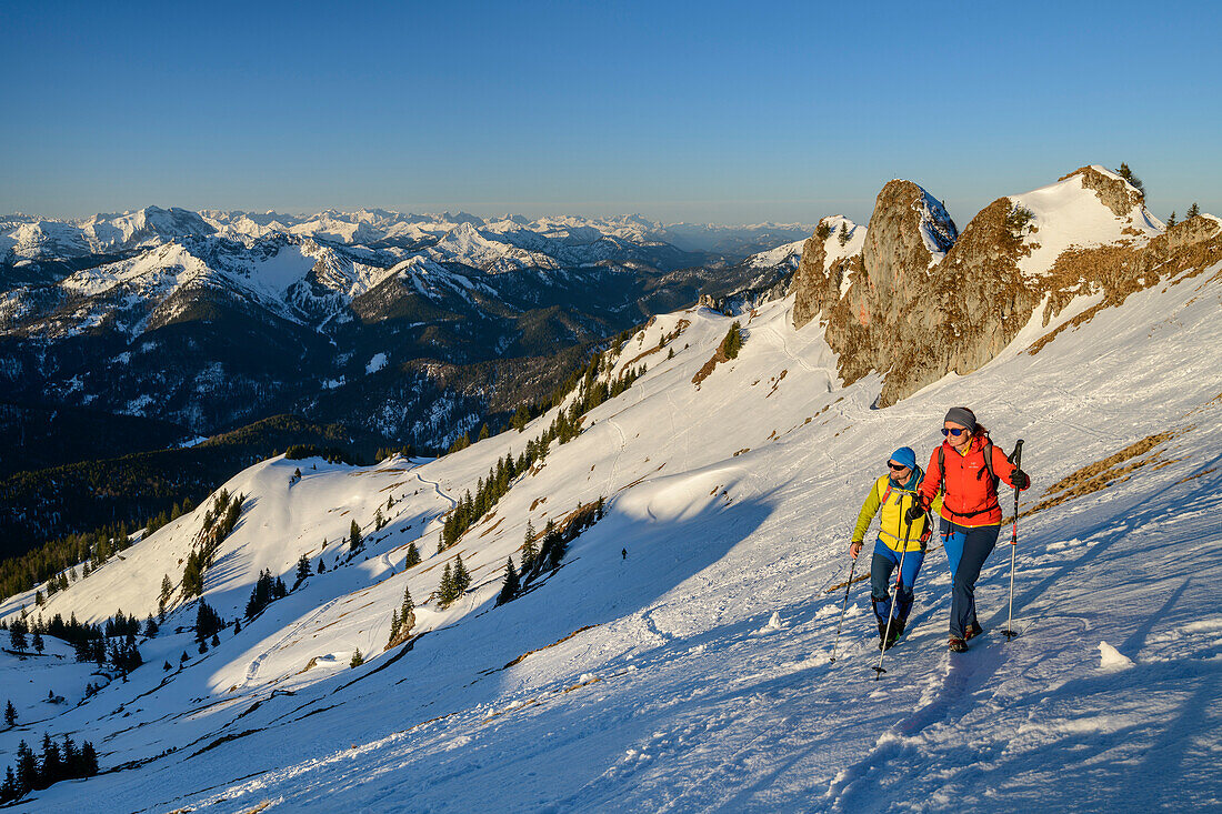 Mann und Frau beim Wandern steigen über Schneehang zur Rotwand auf, Felstürme im Hintergrund, Rotwand, Spitzinggebiet, Bayerische Alpen, Oberbayern, Bayern, Deutschland