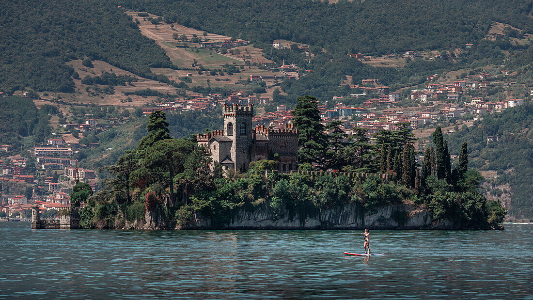Frau paddelt auf SUP Board vor Schloss Castello della Isola di Loreto auf Insel im Iseosee in Italien