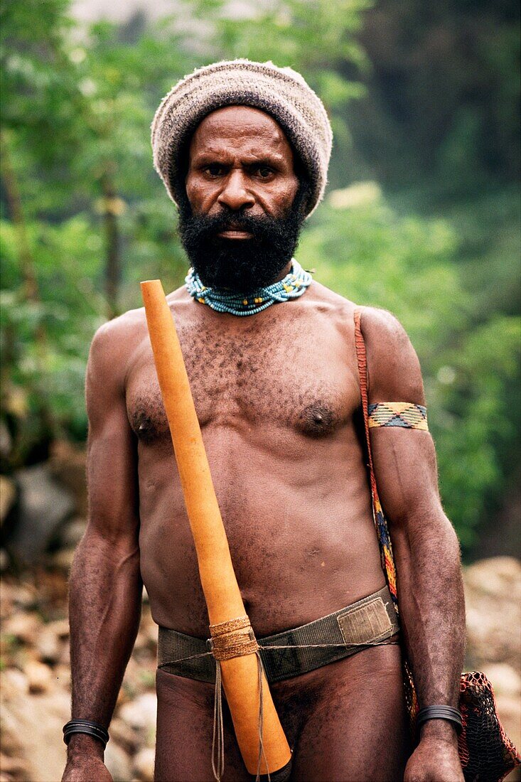 Indigener Mann, der eine Wollmütze trägt und eine Stricktasche über der Schulter trägt, an der Taille ein Kürbis befestigt ist, Irian Jaya, Neuguinea, Indonesien