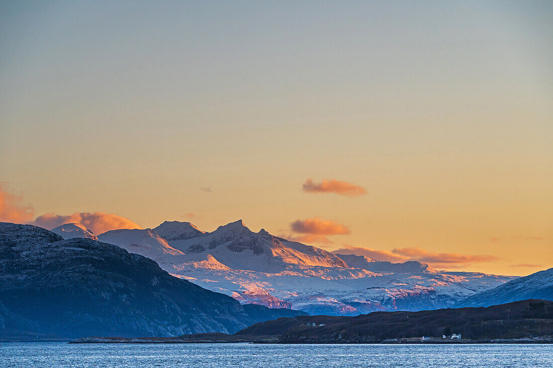Häuser am Polarkreis mit von der Sonnen angestrahlten Bergen im Morgenlicht, Nordland, Norwegen, Europa