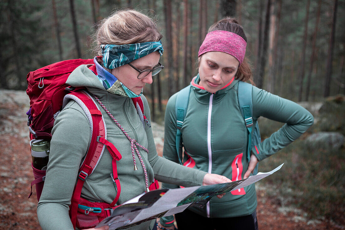Zwei Frauen lesen Wanderkarte beim Wandern im Wald im Tiveden Nationalpark in Schweden\n