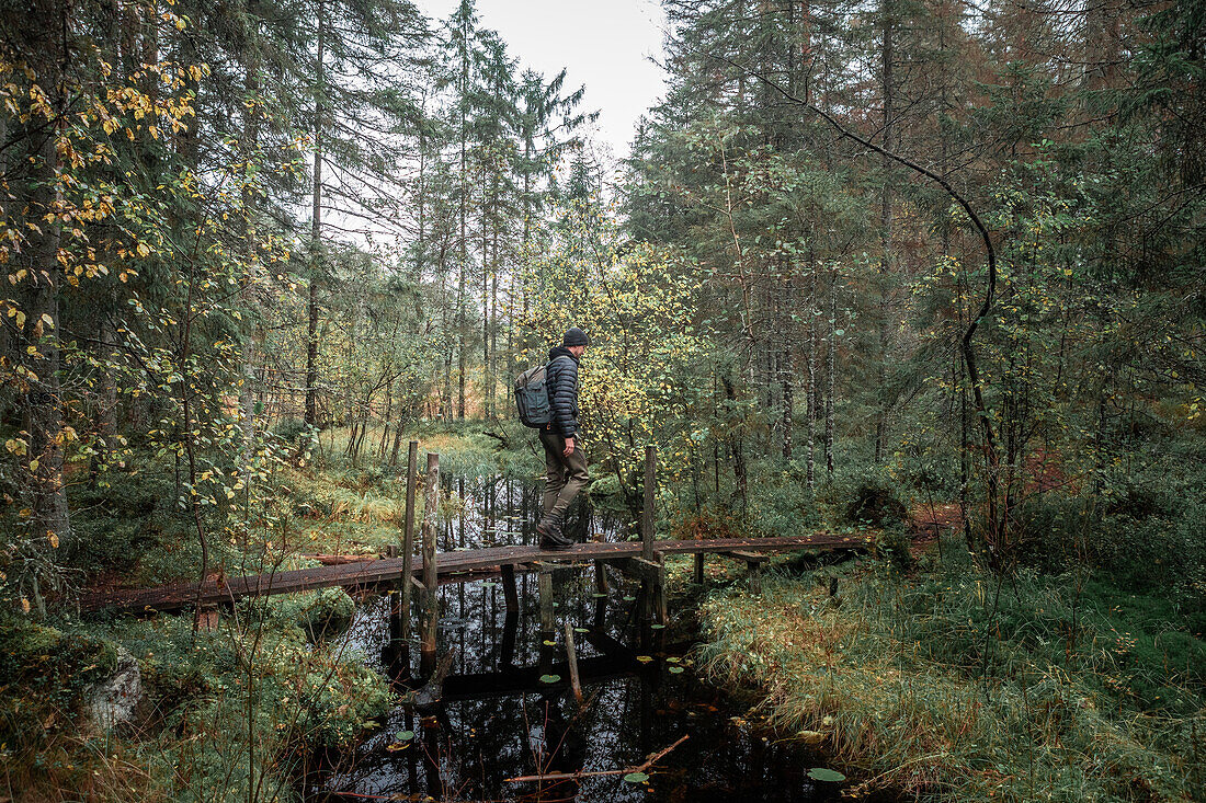 Man with backpack hikes over small bridge of a river in the forest in Tiveden National Park in Sweden