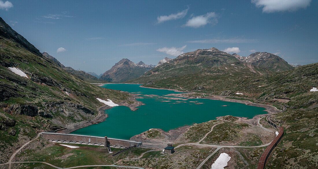 Dam of the Lago Bianco reservoir at the Bernina Pass in the sun from above