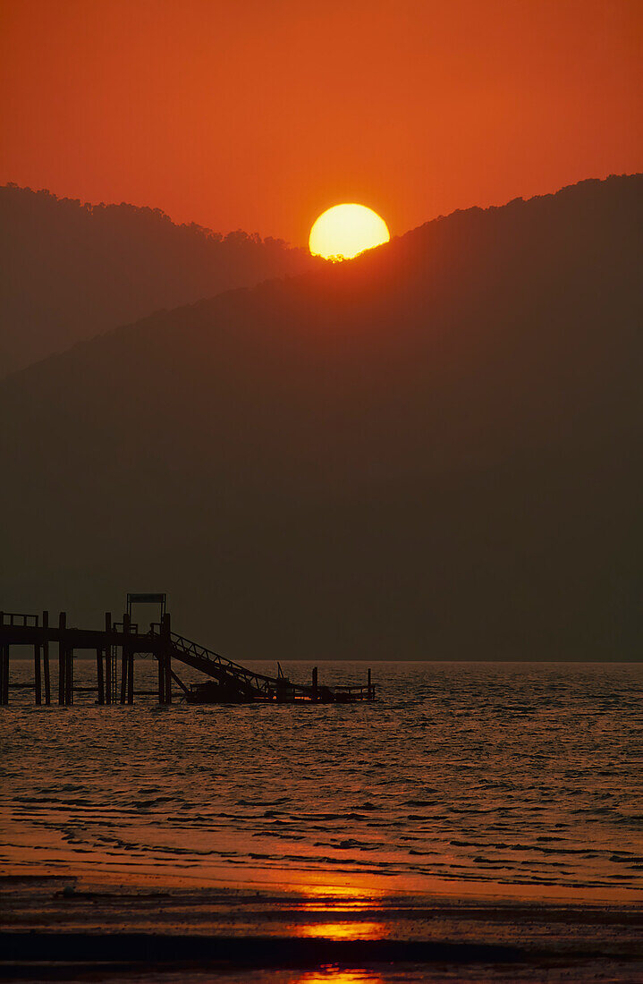 Sonnenuntergang hinter den Hügeln und Jetty auf dem Wasser