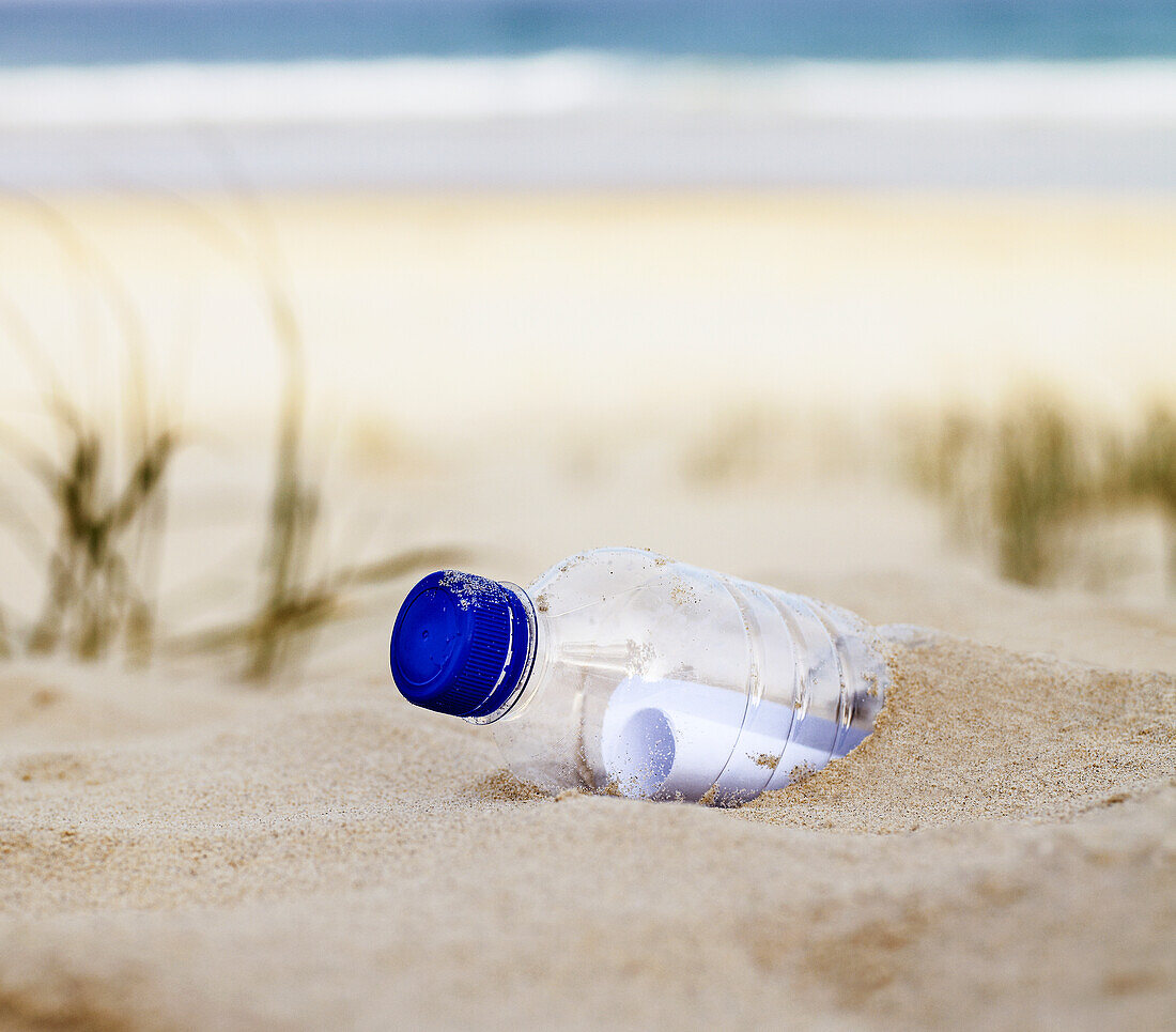 Close up of plastic drink bottle with message in it half buried in sand