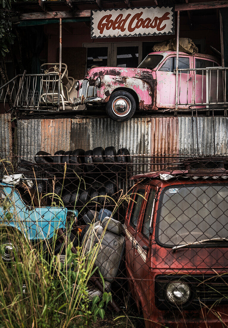 Car Wrecker Yard und rosafarbenes Gebäude mit Autowrack auf dem Balkon im Obergeschoss