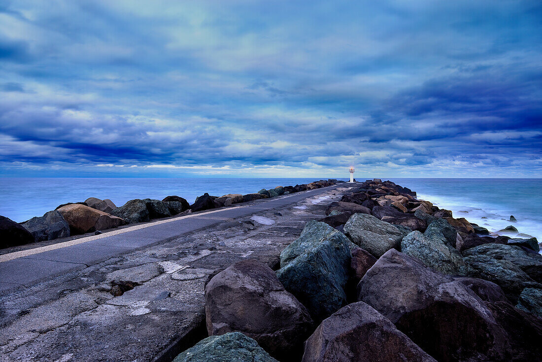 Blick auf die Länge des felsigen Wellenbrechers, der zum Meer führt, am Abend