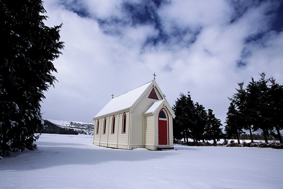 Alte Holzkirche mit roter Tür unter verschneiter Landschaft