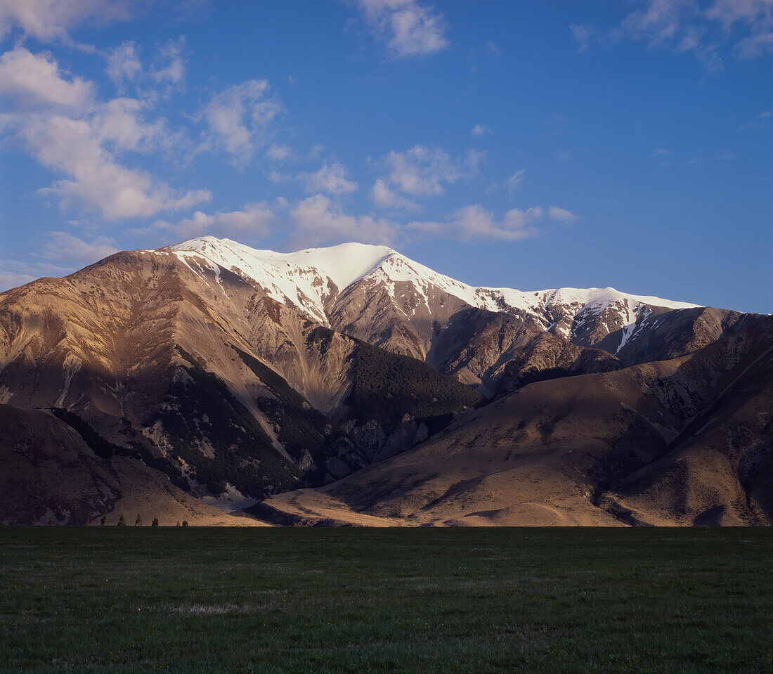 Snow capped mountains meeting the green grassy flat land at Porters Pass in the South Island of New Zealand