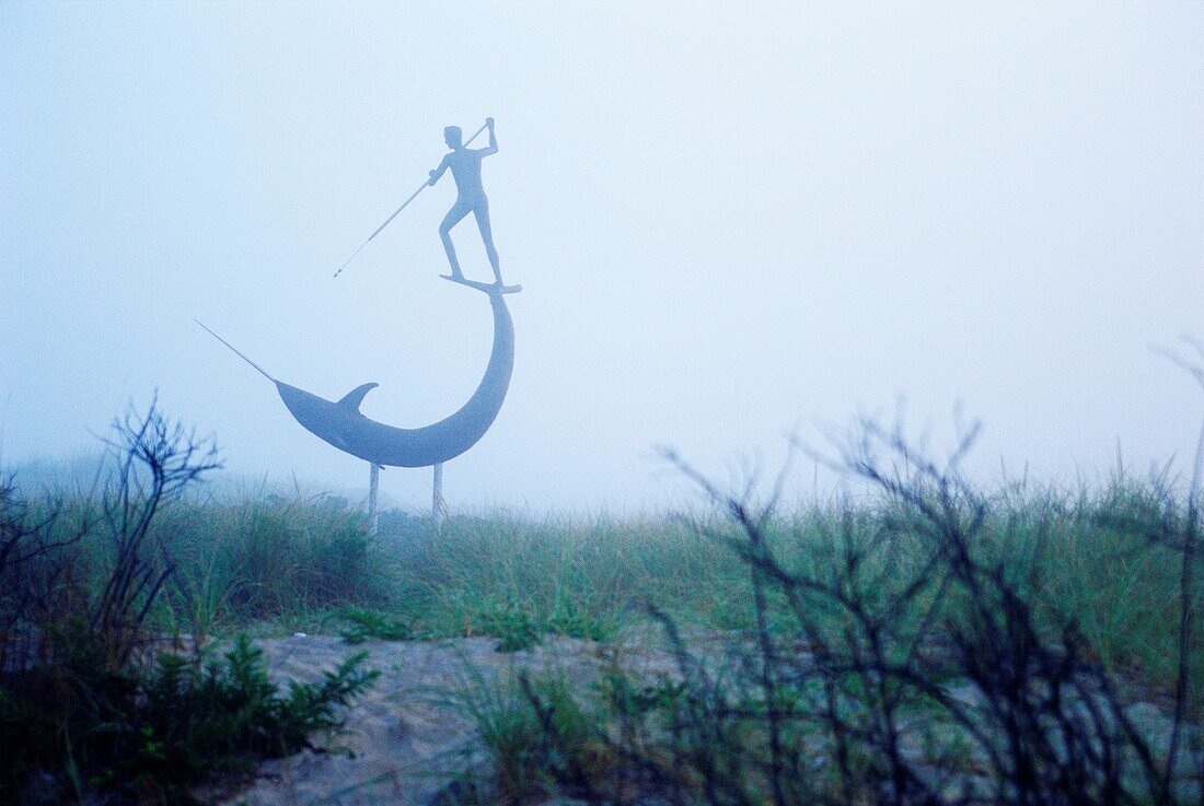 Skulptur, die einen Mann darstellt, der einen Narwal an einem nebligen Strand im Hafen von Menemsha, Martha's Vineyard, Dukes County, Massachusetts, USA, harpuniert