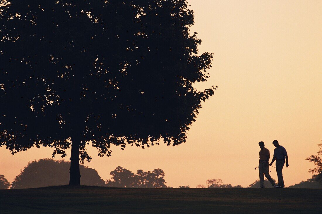 Silhouette von zwei männlichen Golfern auf dem Golfplatz bei Sonnenaufgang