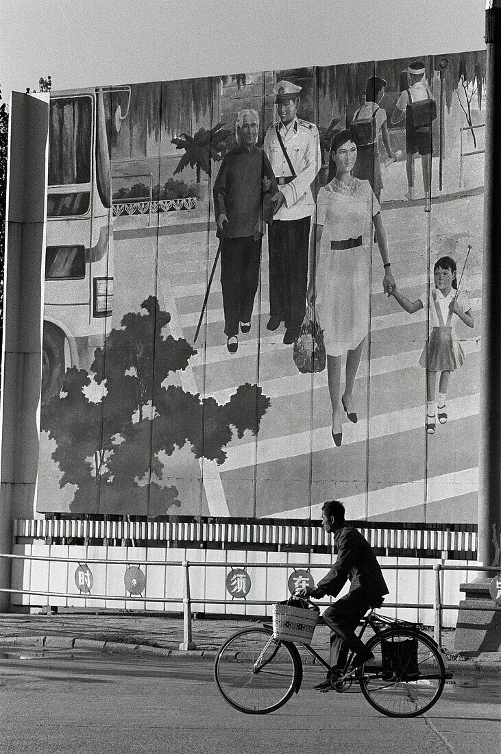Man riding a bicycle in front of a mural, China