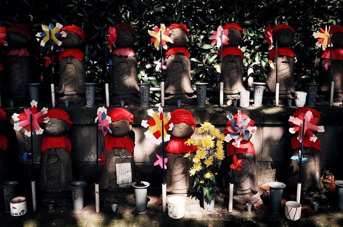Reihen von Statuen von Jizo Bosatsu, verziert mit Strickmützen und Lätzchen und Windrädern, um verstorbene Kinder auf einem Friedhof in Tokio, Japan, darzustellen