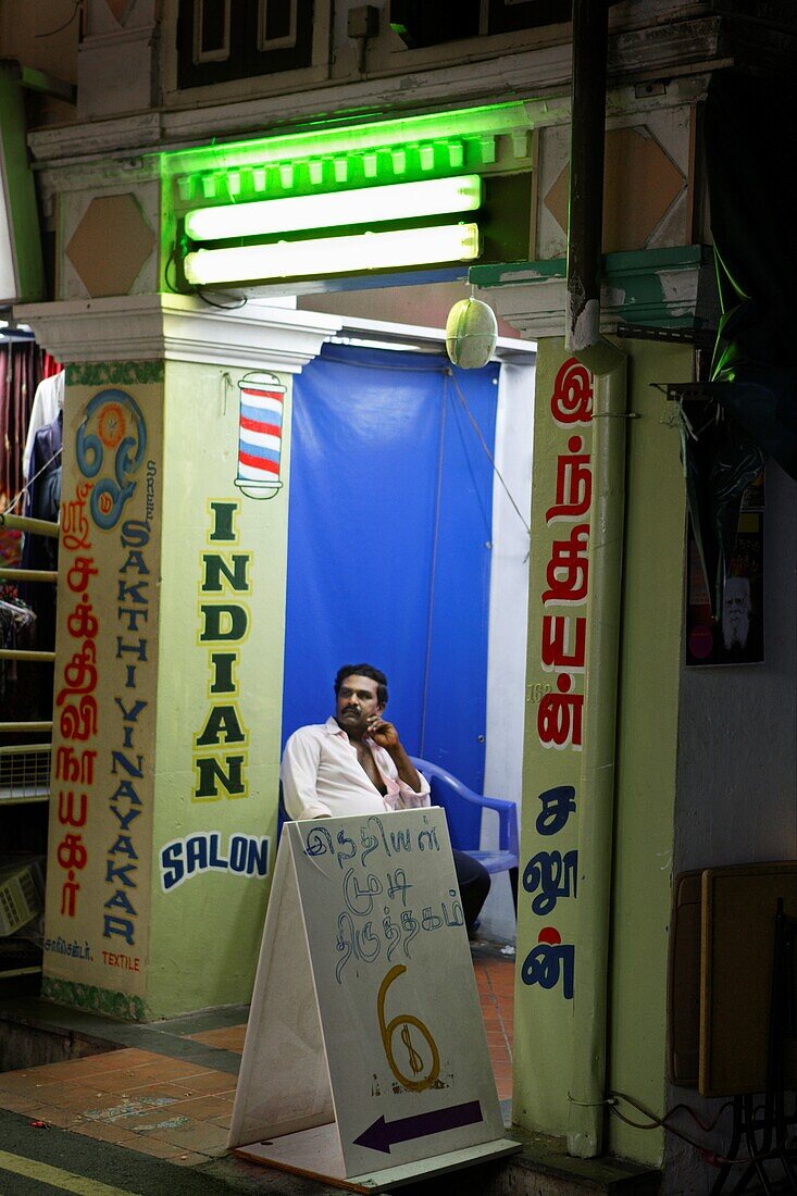 Mann sitzt vor der Tür eines Salons, Little India, Singapur