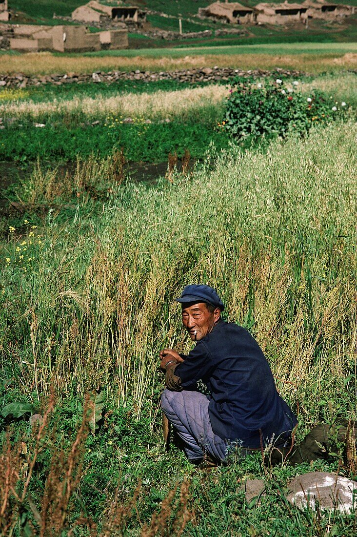 Mann raucht eine Zigarette, während er auf einem Feld sitzt, China