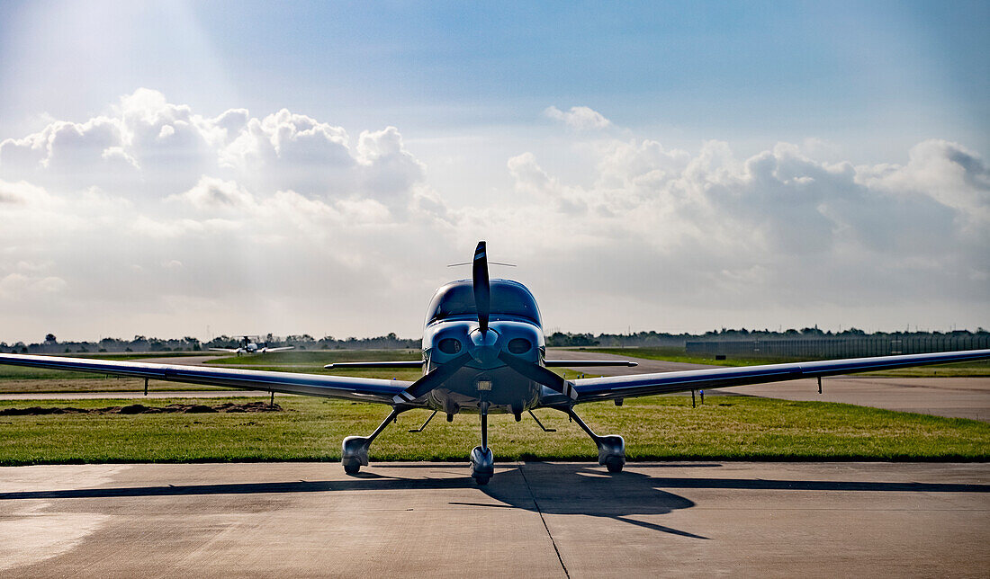 Ein einmotoriges Flugzeug auf einem Flugplatz, während in der Ferne ein Jet abhebt