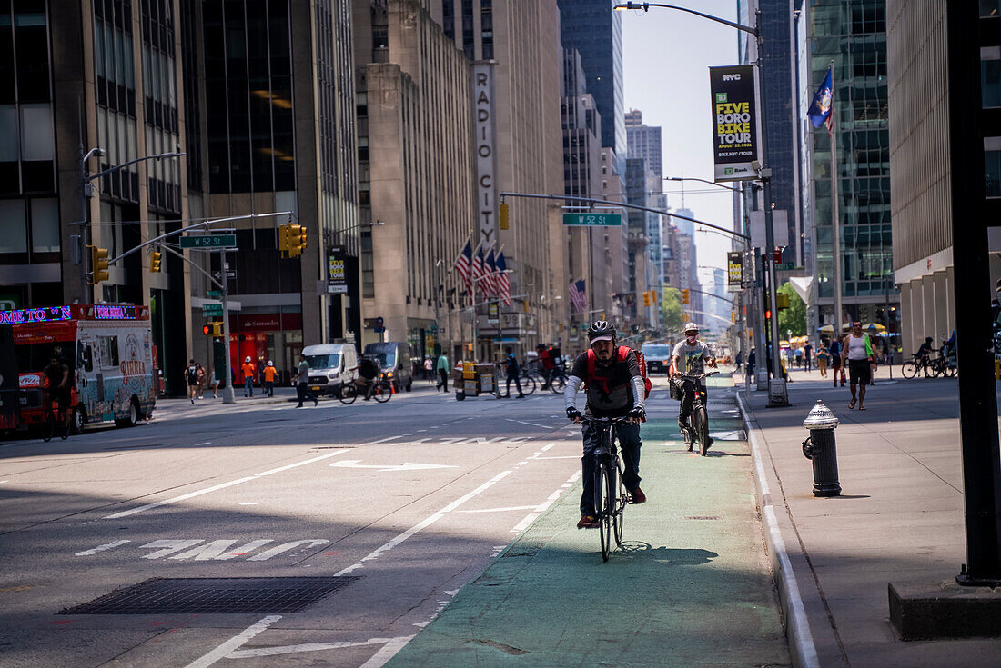 Ein Radfahrer, der die 6th Avenue vor der Radio City Music Hall hinunterfährt, und ein Imbisswagen in Manhattan, New York City.