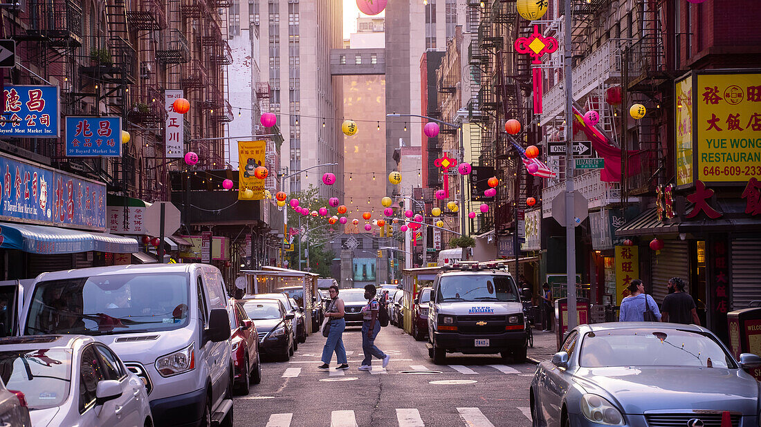 Two people crossing the street in China Town, Manhattan, New York, at sunset.