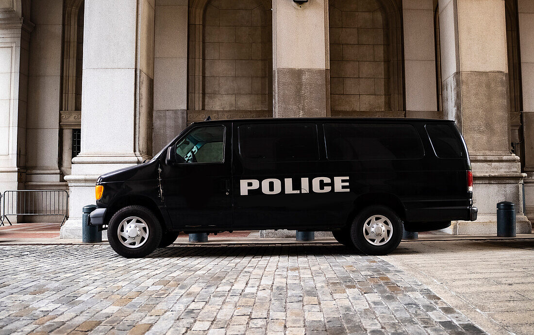 A black police van parked near New York City Hall and the Tweed Courthouse and Comptroller in Manhattan.