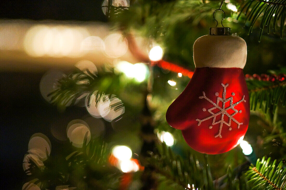 Mitten Ornament with snowflake decoration set against Christmas lights and tree.