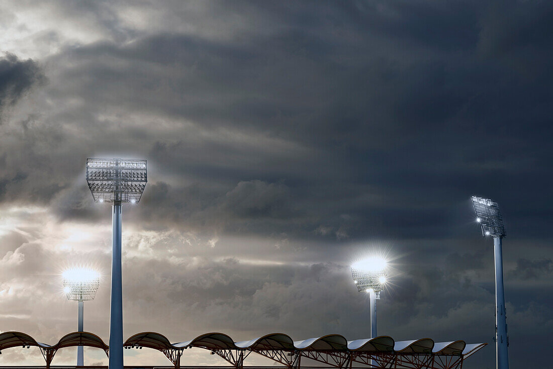 Floodlights shining down into Metricon Stadium on a cloudy evening
