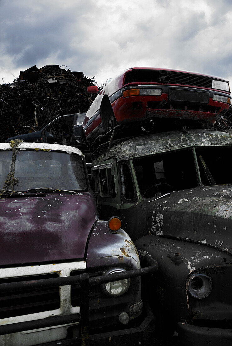 Close up of wrecking yard full of car, truck wrecks, and scrap metal piles against a stormy sky.
