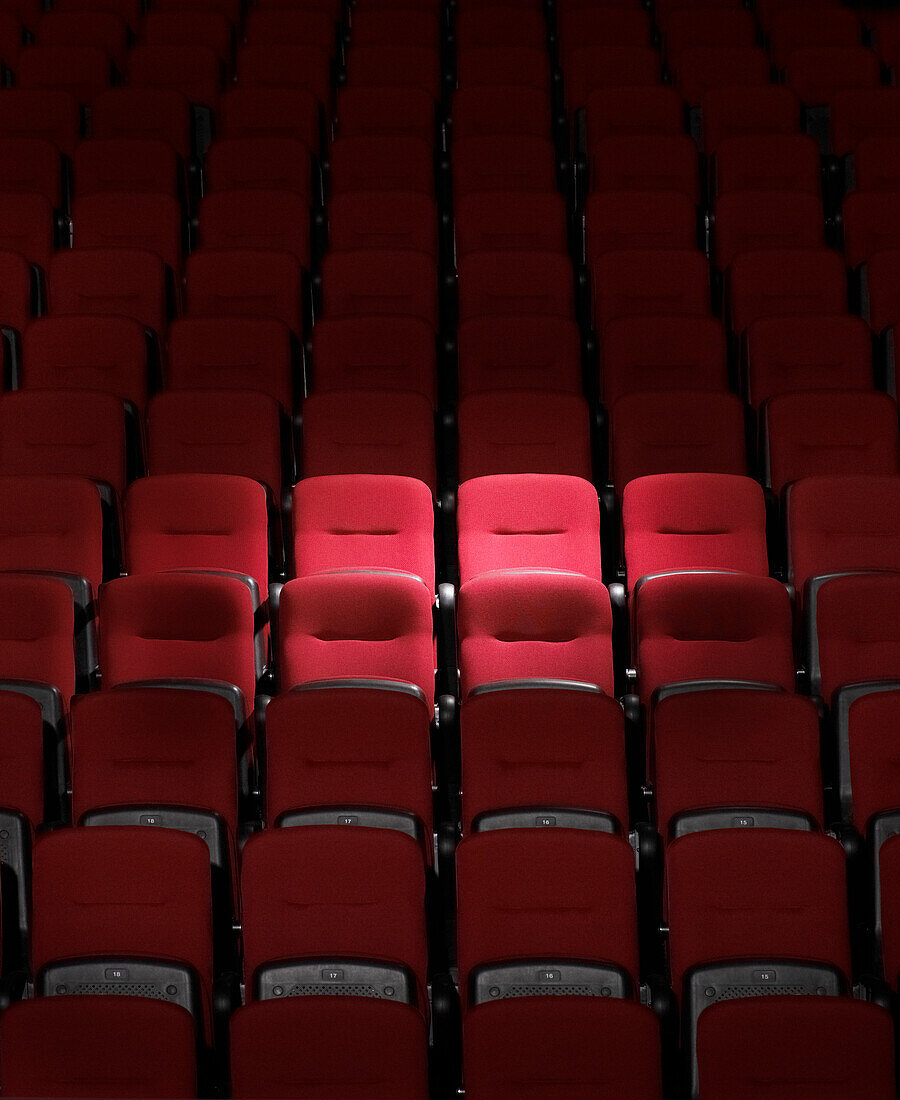 Punktlicht, das auf ein paar rote Sitze in Sitzreihen im Auditorium scheint