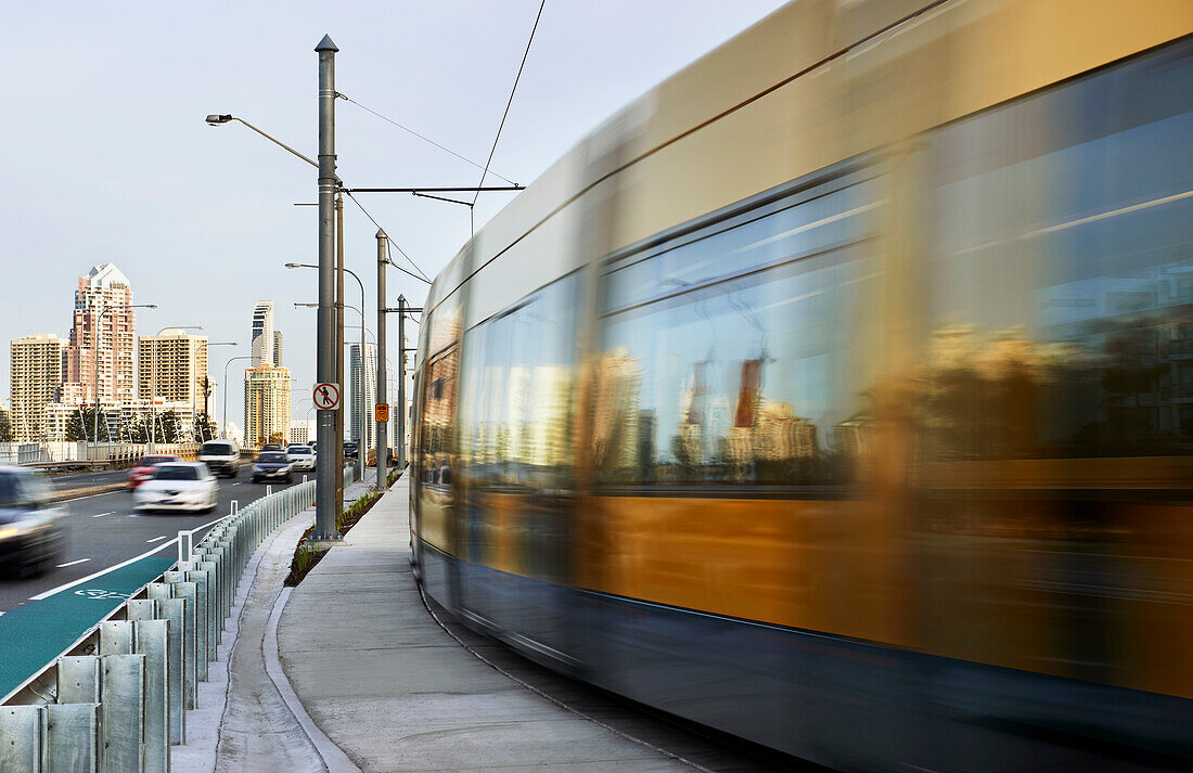 Tram travelling alongside road and Surfers Paradise city in the background